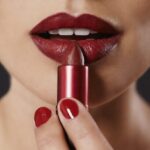 Close-up of a person applying red lipstick from a metallic tube.