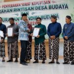 Group of people in traditional Indonesian attire on a stage, exchanging certificates during a cultural awards ceremony.
