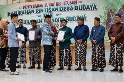 Group of people in traditional Indonesian attire on a stage, exchanging certificates during a cultural awards ceremony.