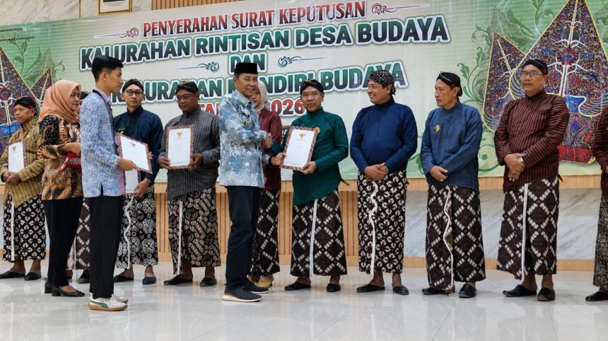 Group of people in traditional Indonesian attire on a stage, exchanging certificates during a cultural awards ceremony.