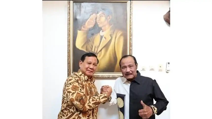 Two men shake hands in front of a large framed painting on a white wall behind them.