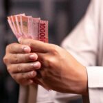A person holding a fanned stack of red 1,000 rupiah banknotes between their fingers.