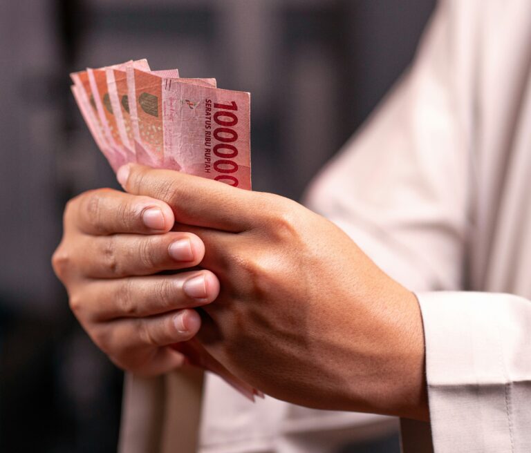 defrino-maasy-izwIqdA4FTU-unsplash - Mabur.co A person holding a fanned stack of red 1,000 rupiah banknotes between their fingers.