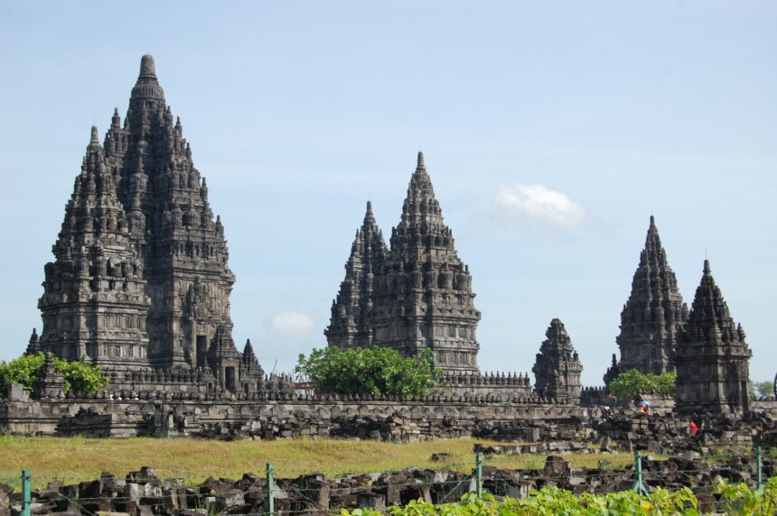 denysabri-temple-598969 - Mabur.co Stone temple complex with tall, stepped spires rising above a low stone wall under a blue sky (Borobudur-like temple).