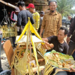 Group of men around an outdoor street food stall, serving fried snacks displayed on banana leaves.