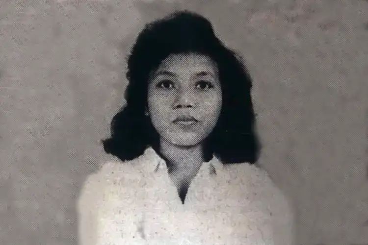 Black-and-white portrait of a woman with shoulder-length dark hair wearing a white blouse, facing the camera with a neutral expression in a studio setting.