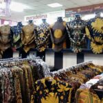 Rows of colorful batik shirts on hangers and mannequins in a busy clothing store nearby racks of patterned shirts in a textile shop.