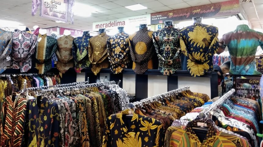 Rows of colorful batik shirts on hangers and mannequins in a busy clothing store nearby racks of patterned shirts in a textile shop.