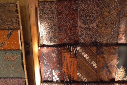 Display of batik fabric rolls in warm earth tones with intricate floral and geometric patterns on a wall display.