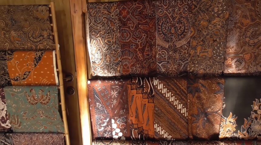 display batik di kampung giriloyo 2 FIXX - Mabur.co Display of batik fabric rolls in warm earth tones with intricate floral and geometric patterns on a wall display.