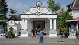 White ornate temple gate with a clock at the top, blue sky above, and visitors standing in front.
