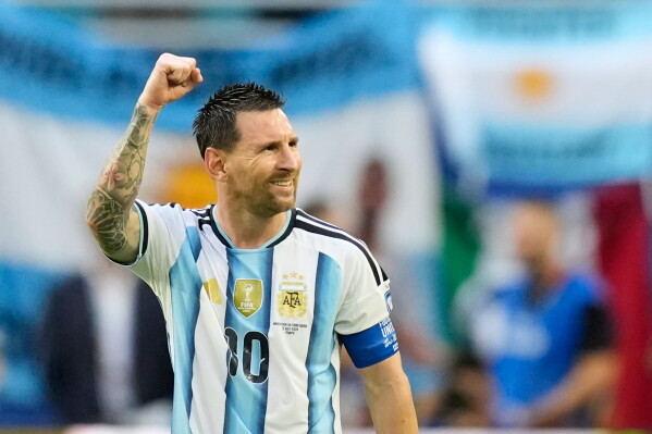 download - Mabur.co Argentine soccer player in a blue-and-white striped jersey raises a clenched fist in celebration on the field, wearing a captain's armband.