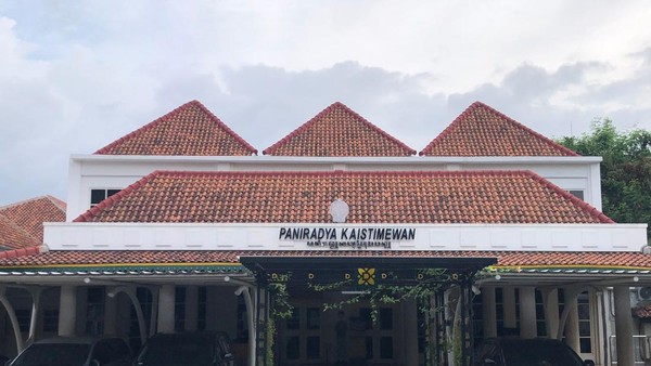 Front view of a low, white building with multiple red-tiled gabled roofs and a covered entrance with a sign above the doors.