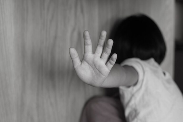 Child with an outstretched hand pressed against a wall, facing away in black and white.