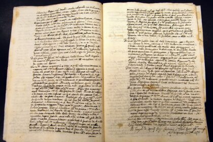Open two-page spread of an antique manuscript with dense cursive handwriting and yellowed, stained pages on a dark background.