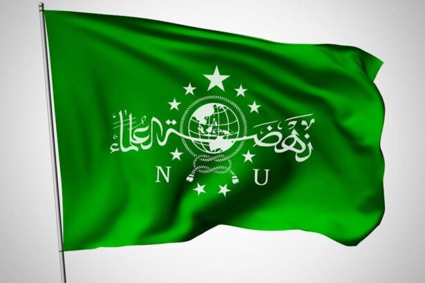 Green flag with a white globe emblem, rope knot, stars, and Arabic script across the center, flapping in wind.