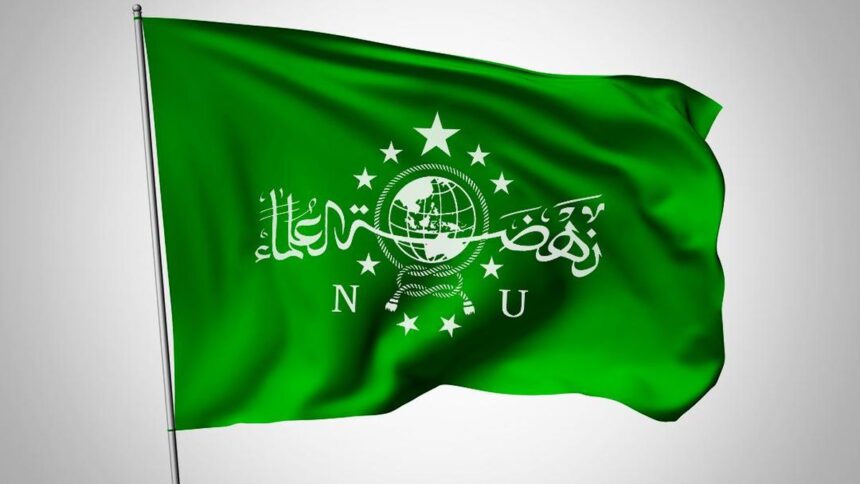 Green flag with a white globe emblem, rope knot, stars, and Arabic script across the center, flapping in wind.