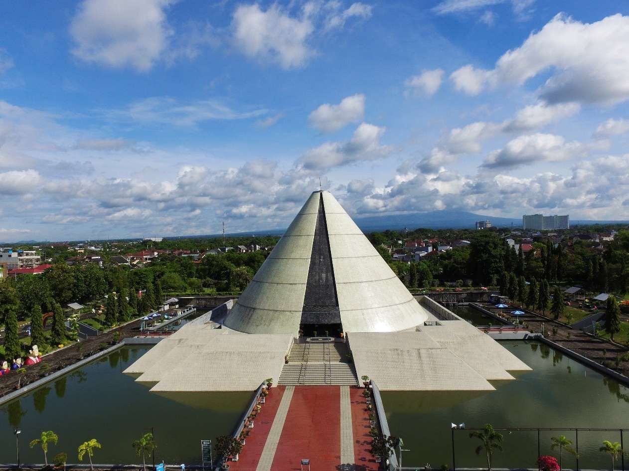 Pyramid-shaped white temple rising from a platform, surrounded by a rectangular moat and a red-carpeted walkway leading to stairs under a blue sky.