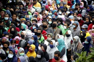 Large diverse crowd wearing face masks outdoors, standing close together.