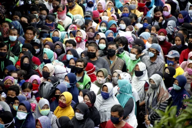 Large diverse crowd wearing face masks outdoors, standing close together.