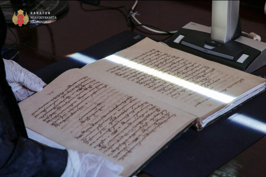 Open antique manuscript with dense handwritten text on a desk; gloved hands and a scanning device nearby.