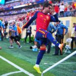 Soccer player in red Spain kit jumping over a barrier as fans cheer in the stadium