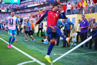 Soccer player in red Spain kit jumping over a barrier as fans cheer in the stadium