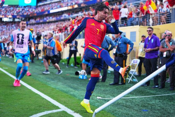 Soccer player in red Spain kit jumping over a barrier as fans cheer in the stadium