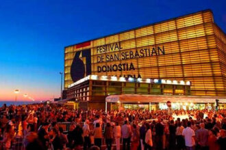 Crowd gathers outside the San Sebastián Film Festival venue at dusk, with the illuminated Donostia building and bold festival signage visible.
