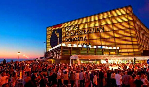 Crowd gathers outside the San Sebastián Film Festival venue at dusk, with the illuminated Donostia building and bold festival signage visible.