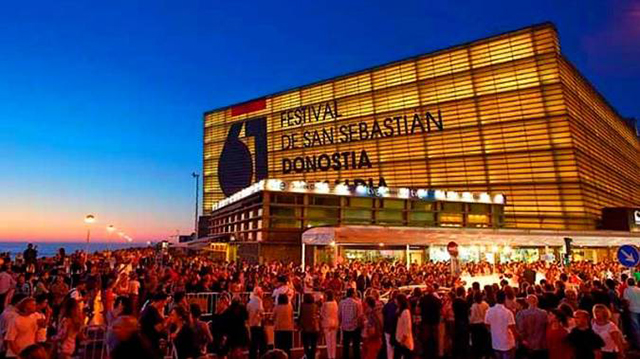 Crowd gathers outside the San Sebastián Film Festival venue at dusk, with the illuminated Donostia building and bold festival signage visible.