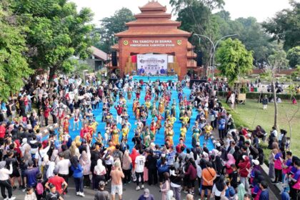 Crowd watches children in colorful traditional costumes perform a parade on a bright blue walkway in front of a brick stage at a cultural festival outdoors.