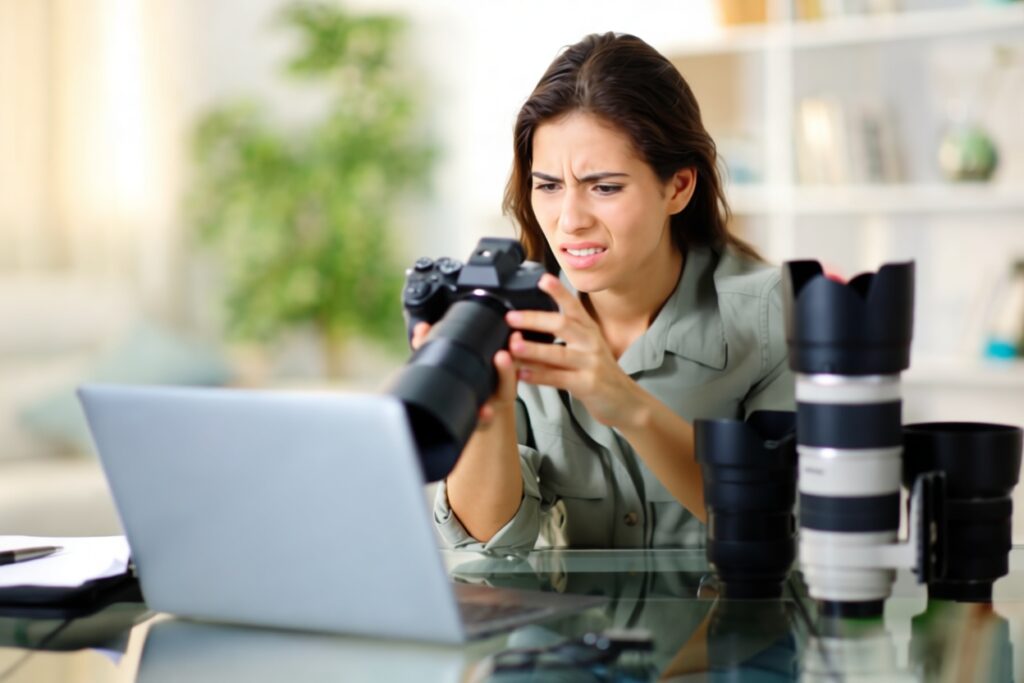 fotografer kesal dgn fotonya sndiri by Getty Images FIXX - Mabur.co Woman examines a DSLR with a telephoto lens on a glass desk, laptop open in front of her, several camera lenses nearby.