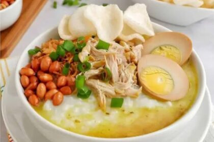 Bowl of creamy congee topped with shredded chicken, halved soft-boiled eggs, peanuts, scallions, and crispy crackers.
