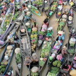 Aerial view of crowded boats at a floating market, vendors selling colorful fruits and vegetables on a muddy river.