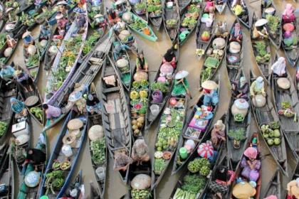 Aerial view of crowded boats at a floating market, vendors selling colorful fruits and vegetables on a muddy river.