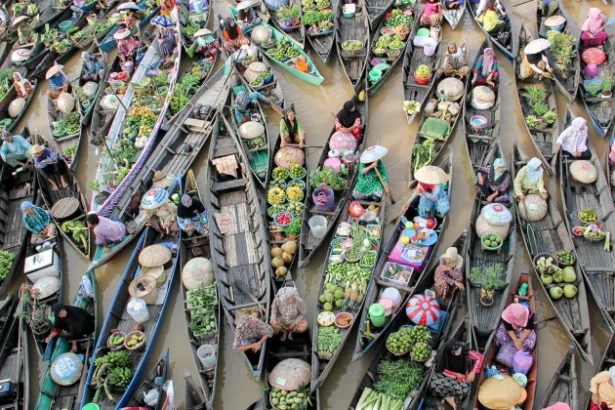 Aerial view of crowded boats at a floating market, vendors selling colorful fruits and vegetables on a muddy river.