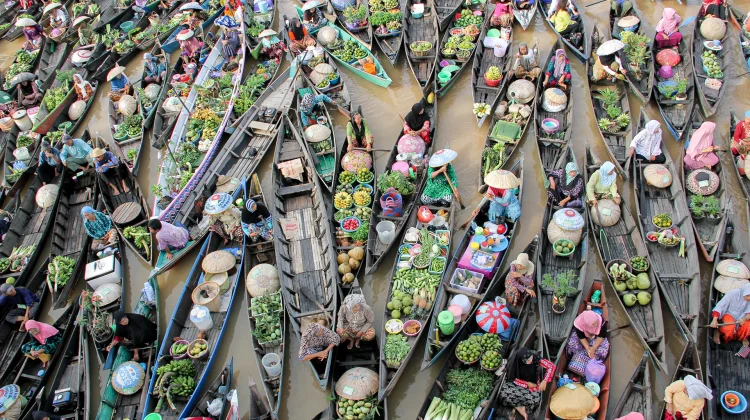 Aerial view of crowded boats at a floating market, vendors selling colorful fruits and vegetables on a muddy river.