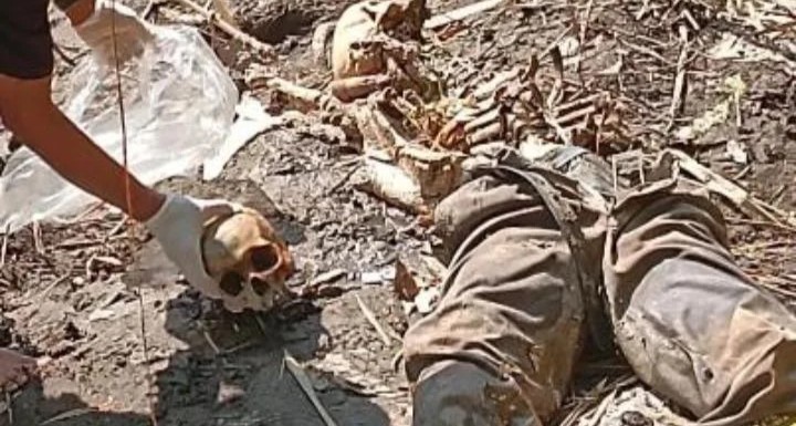 Person lying in rubble with a gloved hand reaching toward a skull among the debris