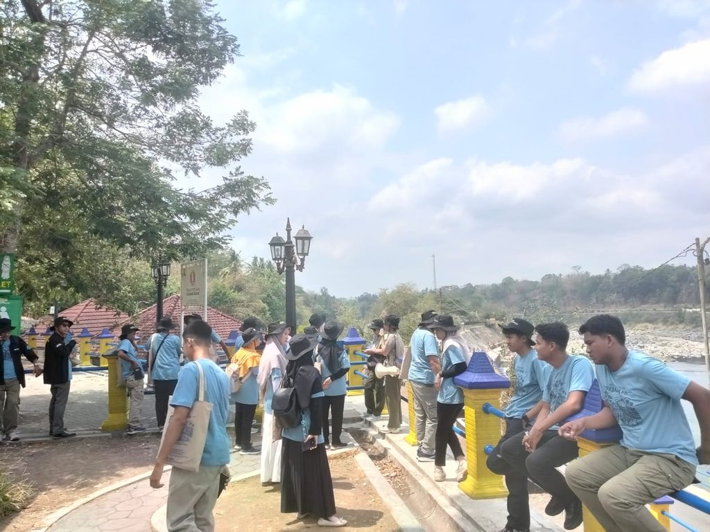 Tour group along a riverside promenade, several people in light blue shirts leaning on a yellow railing under a sunny sky.