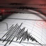 Seismograph recording seismic waves on paper with a needle and jagged lines, red circular patterns in the background.