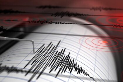 Seismograph recording seismic waves on paper with a needle and jagged lines, red circular patterns in the background.