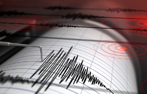 Seismograph recording seismic waves on paper with a needle and jagged lines, red circular patterns in the background.