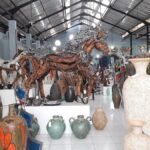 Interior of a pottery shop filled with ceramic vases and a large ornate wooden horse sculpture at the center with silver detailing.