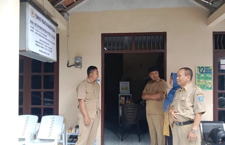 gfxnfg - Mabur.co Four people in beige uniforms stand outside a doorway of a small office, chatting near plastic chairs and a signboard mounted on the wall above.