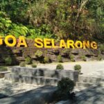 Outdoor sign reading 'GOA SELARONG' in large yellow letters on a stone retaining wall with greenery behind it.