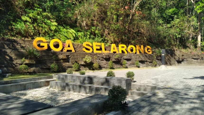 Outdoor sign reading 'GOA SELARONG' in large yellow letters on a stone retaining wall with greenery behind it.