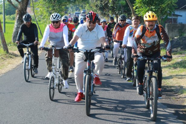Group of cyclists riding together on a rural road, front row wearing helmets and colorful jerseys fallowing a lead rider in white polo.