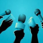 Group of journalists holding microphones up for a question at a press event.