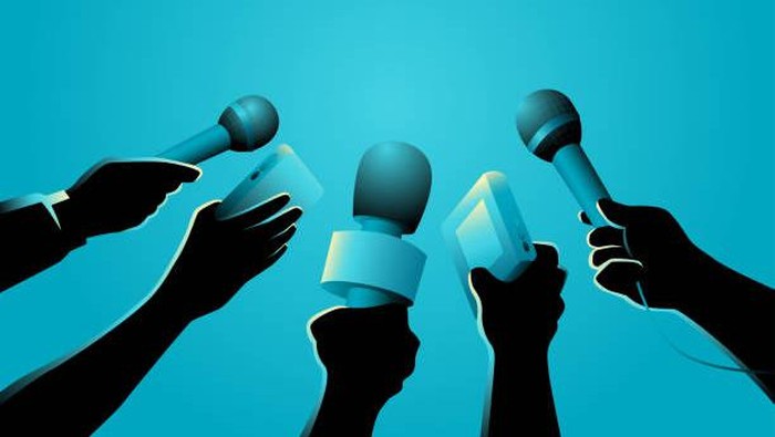 Group of journalists holding microphones up for a question at a press event.